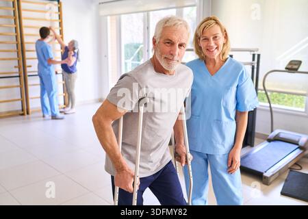 Seniorenmann mit Krücken mit seinem Physiotherapeuten in einem Rehabilitationszentrum Indoor Rehabilitation nach Verletzung das Bild zeigt die Genesung Healthca Stockfoto
