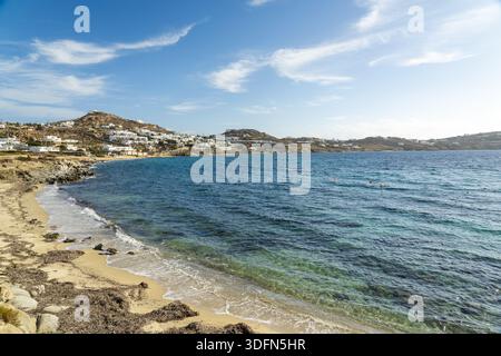 Der Blick auf türkisfarbenes Wasser trifft auf Sandstrände unter hellem Himmel, mit weißen Gebäuden auf den fernen Hügeln, die ein ruhiges Küstenpanorama schaffen, Myk Stockfoto