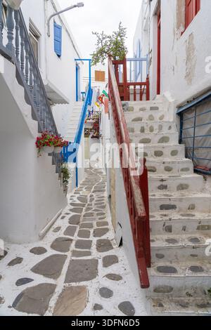 Blick auf die engen kopfsteingepflasterten Gassen, die sich zwischen weiß getünchten Gebäuden mit leuchtenden blauen und roten Akzenten schlängeln, die Treppen hinauf, Altstadt, Mykonos Stockfoto