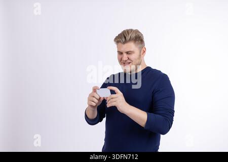 Junger Mann, der leere weiße Kreditkarte hält und in hellem Studio darauf zeigt Stockfoto