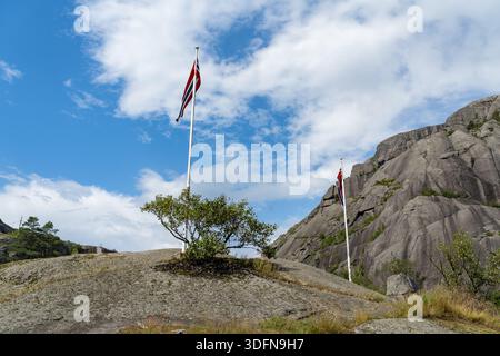 Blick auf die norwegischen Fahnen, die auf felsigen Felsvorsprüngen flattern, vor dem Hintergrund von steilen Klippen und einem riesigen, blauen Himmel mit weißen Wolken, Jossingfjor Stockfoto