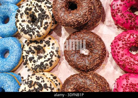 Blick von oben auf verschiedene Donuts mit Schokoladenglasur, Beerenglasur, Zuckerüberzug und Keksbrösel, die auf Backpapier in einer Backstube angeordnet sind Stockfoto