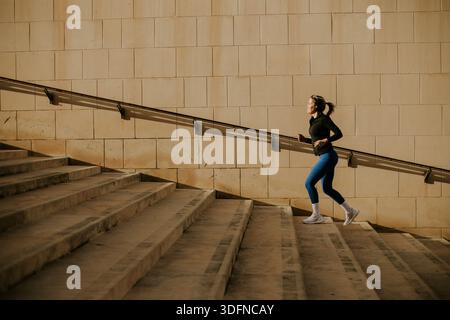 Eine Frau läuft in Malta eine Reihe von Schritten hoch. Sie konzentriert sich auf ihr Workout. Sonnenlicht scheint auf die Treppe und schafft eine helle Morgenszene. Dies Stockfoto