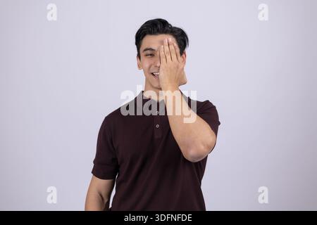 Junger Mann, der ein Auge mit der Hand bedeckt und die Kamera ansieht Stockfoto