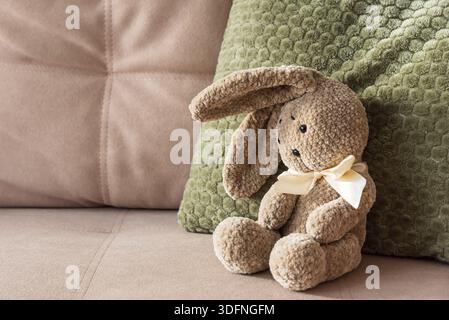 Plüschhase auf Sofa mit grünem Kissen. Gemütlicher, Von Kindheit Inspirierter Hintergrund Stockfoto