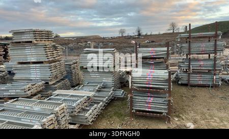 Baustelle mit gestapelten Gerüstplanken und Rohren aus Metall. Der Himmel ist bewölkt und grau. Stockfoto