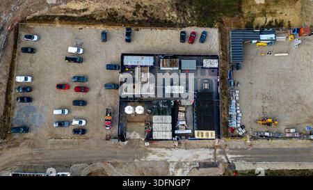 Luftaufnahme einer Baustelle mit modularen Gebäuden, geparkten Fahrzeugen und Baumaterialien vor dem Hintergrund von Schmutz und Kies bei T Stockfoto