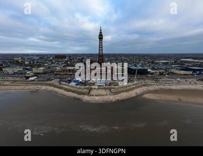 Aus der Vogelperspektive auf eine Küstenstadt mit einem markanten Turm, einer Promenade, Fahrgeschäften im Vergnügungspark und einem Strand unter einem bewölkten Himmel in Blackpool Stockfoto