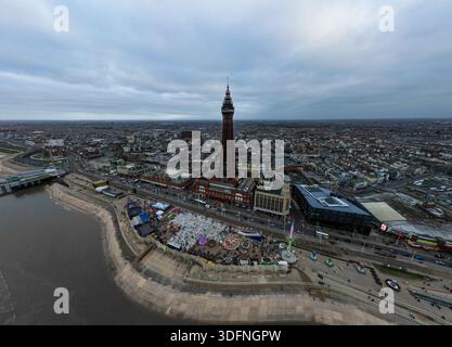 Aus der Vogelperspektive auf eine Küstenstadt mit einem markanten Turm und einem lebhaften Vergnügungsviertel am Ufer, unter einem bewölkten Himmel. Stockfoto