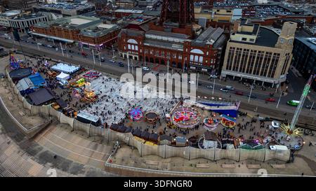 Ein Blick aus der Vogelperspektive auf einen belebten Vergnügungsbereich am Meer mit Fahrgeschäften, Verkaufsständen und Menschen. Der berühmte Blackpool Tower ist im Hintergrund zu sehen. Stockfoto