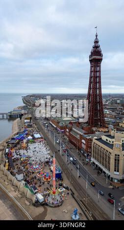 Ein Blick aus der Vogelperspektive auf eine Küstenstadt mit einem markanten Eisenturm, einem belebten Vergnügungsviertel und einer Strandpromenade unter bewölktem Himmel. Stockfoto