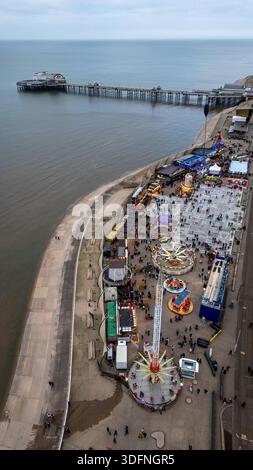 Aus der Vogelperspektive auf einen Vergnügungspark am Meer mit einem Pier in der Ferne, mit verschiedenen Fahrgeschäften, Ständen und einer Menschenmenge in Blackpool Stockfoto
