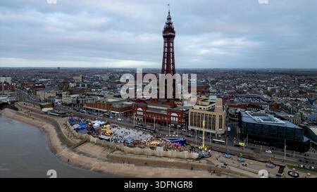 Ein Blick aus der Vogelperspektive zeigt eine Küstenstadt mit einem markanten Eisenturm, Fahrgeschäften im Vergnügungspark und eine Stadtlandschaft unter einem bewölkten Himmel in Blackpool. Stockfoto