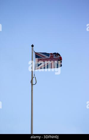 Eine zerrissene Union Jack-Flagge flattert vor einem klaren, hellblauen Himmel, montiert auf einem Metallfahnenmast mit einem dekorativen Finial in Edinburgh, Schottland. Stockfoto