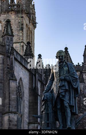 Eine Statue eines Mannes in Kleidung aus dem 18. Jahrhundert steht vor einem gotischen Steinbau. Der Himmel ist in Edinburgh, Schottland, klar, blassblau. Stockfoto