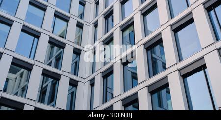 Moderne Bürofassade mit Glasfenstern und Metallpaneelen, die ein klares geometrisches Architekturmuster für den Unternehmenshintergrund bilden. Stockfoto