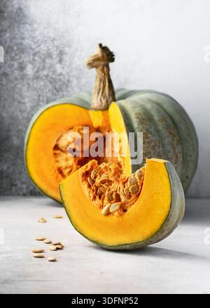 Bio-Kürbis „Crown Prince“ (Cucurbita maxima) mit geschliffenem Keil, der leuchtend orangefarbenes Fruchtfleisch und Samen in minimalistischem Stillleben offenbart. Stockfoto