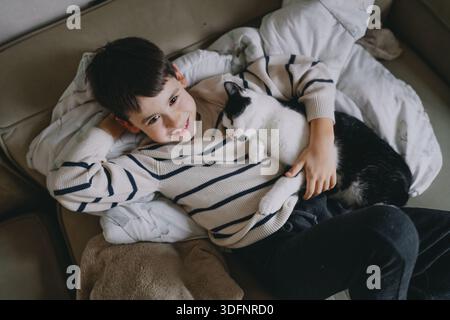 asiatischer Junge kuschelt Smoking Katze auf Sofa verspielter Komfort Stockfoto