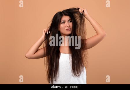 Frustrierte armenische Frau, die ihre beschädigten langen Locken zeigt, schlechte Haare am Tag hat, verärgert über ihre unordentliche Frisur Stockfoto