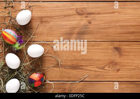 Bunte Ostereier und weiße Eier auf Holzfläche mit Heu Stockfoto