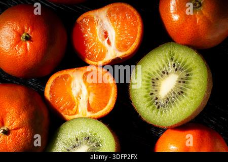 Geschnittene Mandarinen-Kiwi-Mischung auf schwarzem Holzhintergrund von oben Stockfoto