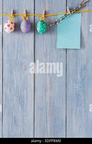 Dekorative, handbemalte Eier hängen an einer Schnur mit blauem Tuch vor hölzernem Hintergrund Stockfoto