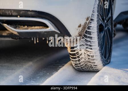 Winterfahrrad und Reifenprofil mit schneebedeckten Rillen, schmutziger Stoßfängerkante und kleinen Eiszapfen darunter, geparktes Fahrzeug auf vereister Schneelage im Freien Stockfoto