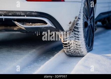 Fahrzeugreifen auf Schnee mit tiefem Profil und vereisten Ansammlungen, Nahsicht auf die Stoßfängerecke mit gefrorenen Tropfen und Slush, die auf rauen Winterstraßen zeigen Stockfoto