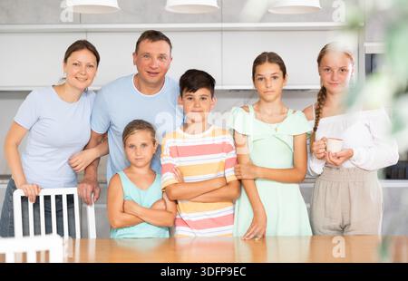 Glücklicher Vater und Mutter mit drei Töchtern und Sohn stehen neben dem Küchentisch. Stockfoto