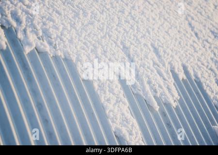 Schneeschicht auf Wellblech, Nahsicht auf Grate und gepackte Schneeränder schaffen abstrakte Wintertextur und Baumaterial bac Stockfoto