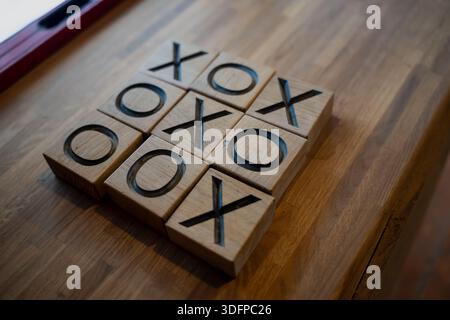 Auf dem Tisch angeordnete Spielblöcke aus Holz mit Tic Tac Toe, Nahaufnahme von geschnitzten X- und O-Symbolen in natürlichen Holzwürfeln mit geringer Schärfentiefe und warmem Licht Stockfoto