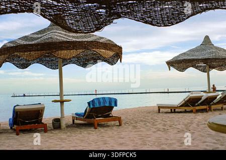 Leere Sonnenliegen unter Strohschirmen am Strand Sharm El Sheikh, Ägypten Stockfoto