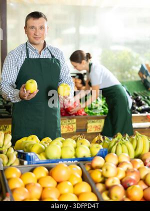 Mann Verkäufer, der im Supermarkt arbeitet und Äpfel auf der Theke verteilt Stockfoto