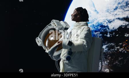 Crew-Mitglied der Orbitalstation bewegt sich von der Schönheit der Erde im Weltraum und freut sich, nach Hause zu gehen. Fröhliche afroamerikanerin, die Emotionen spürt, wenn sie auf den Heimatplaneten zurückblickt, um 360 Grad drehend, Kamera B Stockfoto