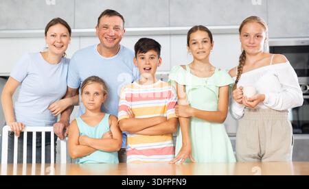 Glücklicher Vater und Mutter mit drei Töchtern und Sohn stehen neben dem Küchentisch. Stockfoto