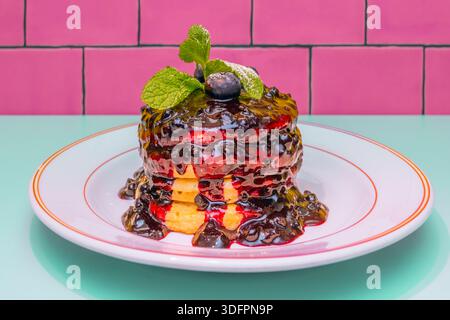 Aus der Vogelperspektive sehen Sie Vollkorn- oder Haferpfannkuchen, großzügig und farbenfroh mit Kiwischeiben, Heidelbeeren, roten Himbeeren und ein paar Minzzweigen Stockfoto