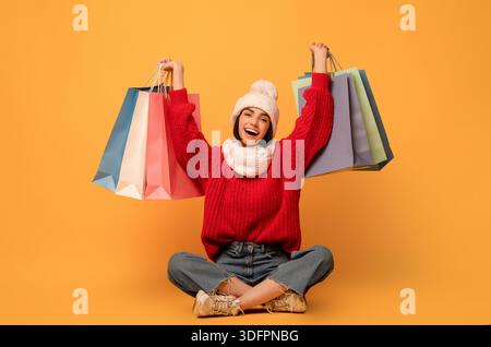 Saisonale Verkäufe. Glückliche Frau hält Einkaufstaschen, sitzt auf gelbem Hintergrund und lächelt in die Kamera Stockfoto