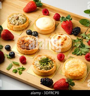 Farbenfrohe Auswahl an süßem Gebäck und frischen Beeren, darunter Erdbeeren, Himbeeren und Brombeeren, serviert auf einem rustikalen Holzbrett Stockfoto