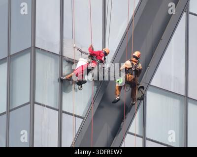 Fensterputzer arbeiten in der Höhe, während sie an Seilen an der Außenseite eines Hochhauses in Yangon, Myanmar, hängen. Stockfoto