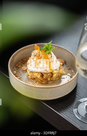 Ein raffiniertes Dessert mit einer Basis aus karamellisierten Äpfeln, garniert mit einem Schuss frischer Schlagsahne, Zitrusschale und Minzblatt. Stockfoto