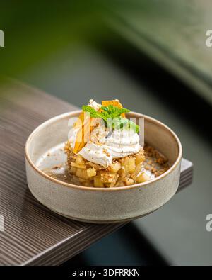 Ein raffiniertes Dessert mit einer Basis aus karamellisierten Äpfeln, garniert mit einem Schuss frischer Schlagsahne, Zitrusschale und Minzblatt. Stockfoto