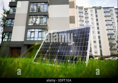 Photovoltaik-Sonnenkollektor vor einem modernen Apartmentgebäude mit Balkonen, die auf eine Wohn- oder Mischnutzung schließen lassen. Konzept der Integration nachhaltiger erneuerbarer Energiequellen in die Architektur. Stockfoto