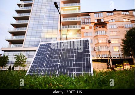 Photovoltaik-Sonnenkollektor vor einem modernen Apartmentgebäude mit Balkonen, die auf eine Wohn- oder Mischnutzung schließen lassen. Konzept der Integration nachhaltiger erneuerbarer Energiequellen in die Architektur. Stockfoto