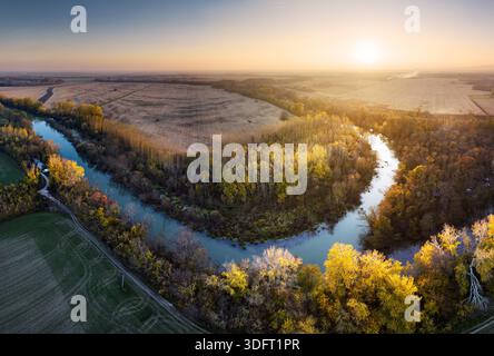 Luftlandschaft gelber Herbstwald mit mäandernem kleinen gewundenen Fluss mit Sonnenlicht, Draufsicht. Stockfoto