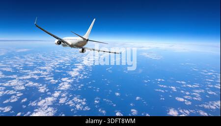 Weißes Flugzeug fliegt über einer riesigen Schicht weißer Wolken unter einem klaren blauen Himmel Stockfoto