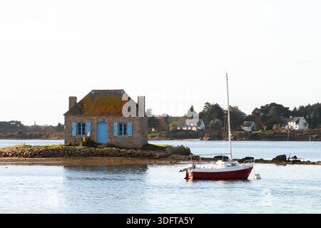 Ein Haus mit blauem Fenster, umgeben von der Seatide und mit einem roten Boot, auf der Insel Saint Cado in der Stadt Belz in der Bretagne, Frankreich Stockfoto