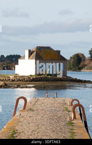 Ein Haus mit blauem Fenster, umgeben von der Seatide, vom Dock, auf der Insel Saint Cado in der Stadt Belz in der Bretagne, Frankreich Stockfoto