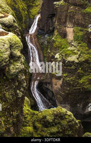 Blick auf einen kaskadierenden Wasserfall, der durch einen moosbedeckten Canyon schneidet, dessen Wasser den Himmel über Fjadrargljufur, Kirkjubaejarklaustur, Sout reflektiert Stockfoto