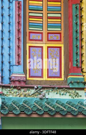 Lebendig gemaltes Heritage-Fenster an einer traditionellen Gebäudefassade in Singapur, mit mehrfarbigen Fensterläden in horizontalen Streifen in Rot, Grün, Stockfoto
