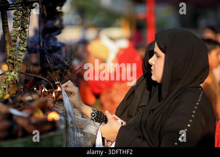 [Lahore], [Pakistan] - 24. Dezember 2025: Blick auf eine Frau in einem schwarzen Hijab, die zart Weihrauchstäbchen anzündet, ihr Gesicht heiter vor dem sanften Leuchten Stockfoto